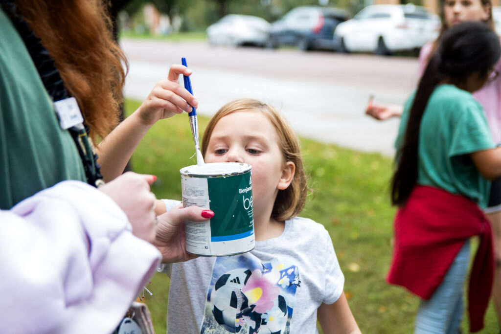 child dipping their paint brush in paint to participate in an activity afterschool